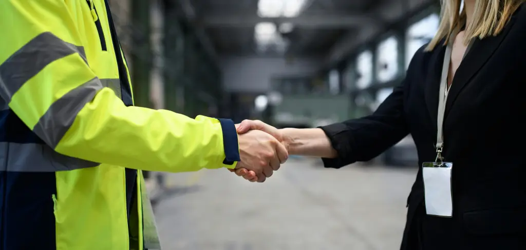 Poignée de main entre un collaborateur en veste de chantier jaune et un autre en costume, dans un environnement industriel